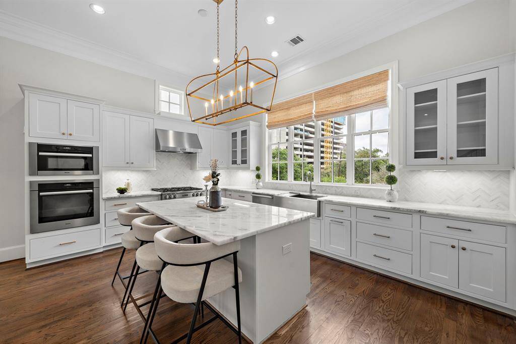 Expansive windows frame downtown views, while a dramatic gold chandelier, chevron backsplash, and hardwood floors create a stunning blend of style and function, ideal for both gourmet cooking and upscale entertaining.