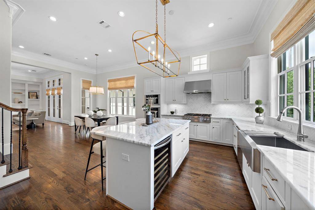 Showcasing high-end designer finishes, this gourmet kitchen boasts an expansive marble island with wine storage, pro-grade stainless gas range, and elegant chevron backsplash.