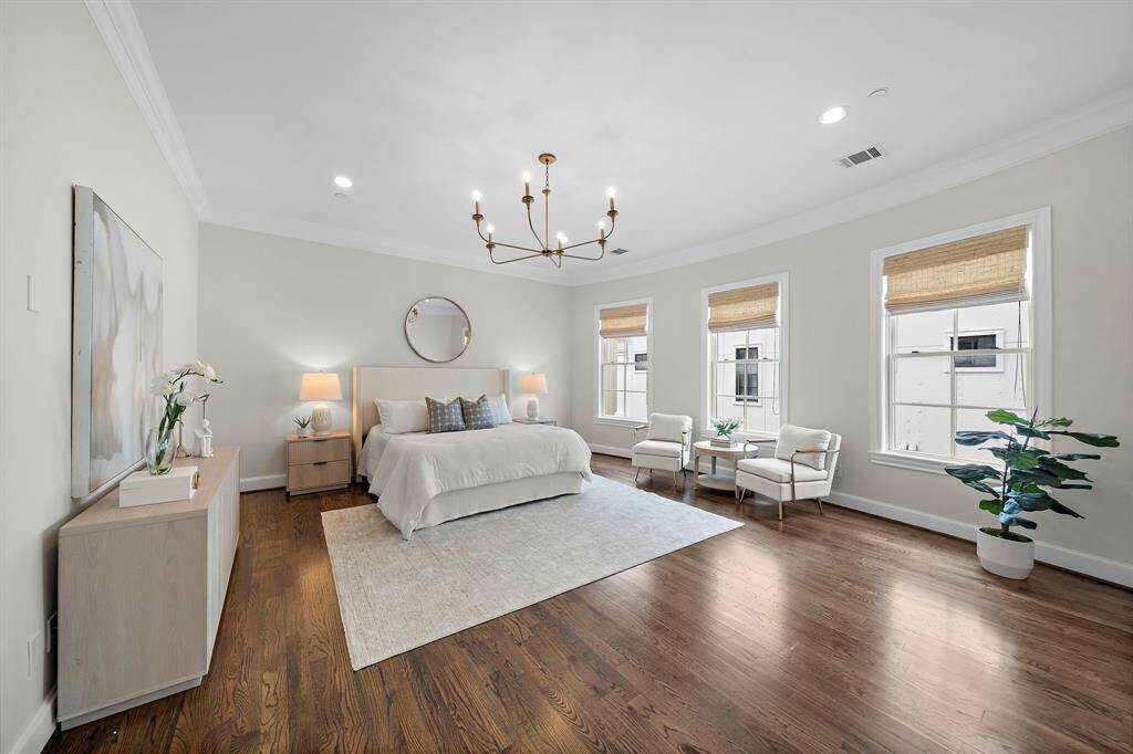 The expansive primary suite features refined hardwood floors, a statement designer chandelier, and abundant natural light from the oversized windows.