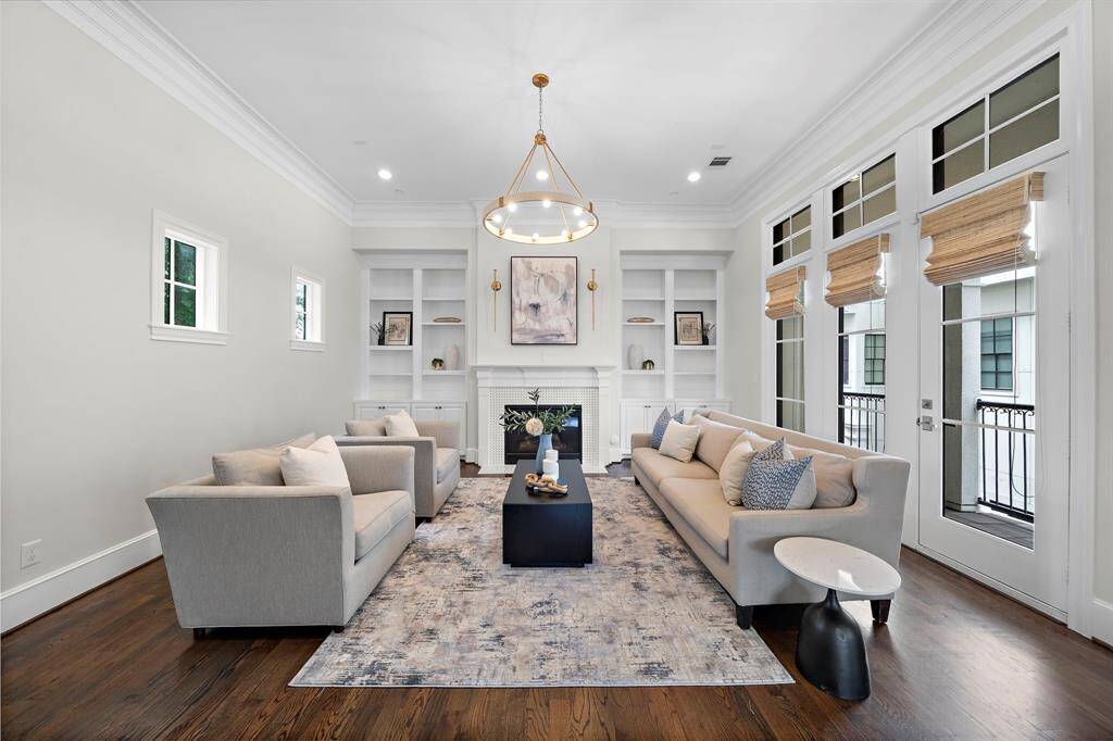 Expansive living room impresses with soaring ceilings, stunning hardwood floors, and designer lighting fixtures. Built-in shelving flanks the sleek fireplace, while oversized windows and French doors bathe the space in natural light and grant private balcony access—an ideal retreat for luxurious relaxation or elegant entertaining.