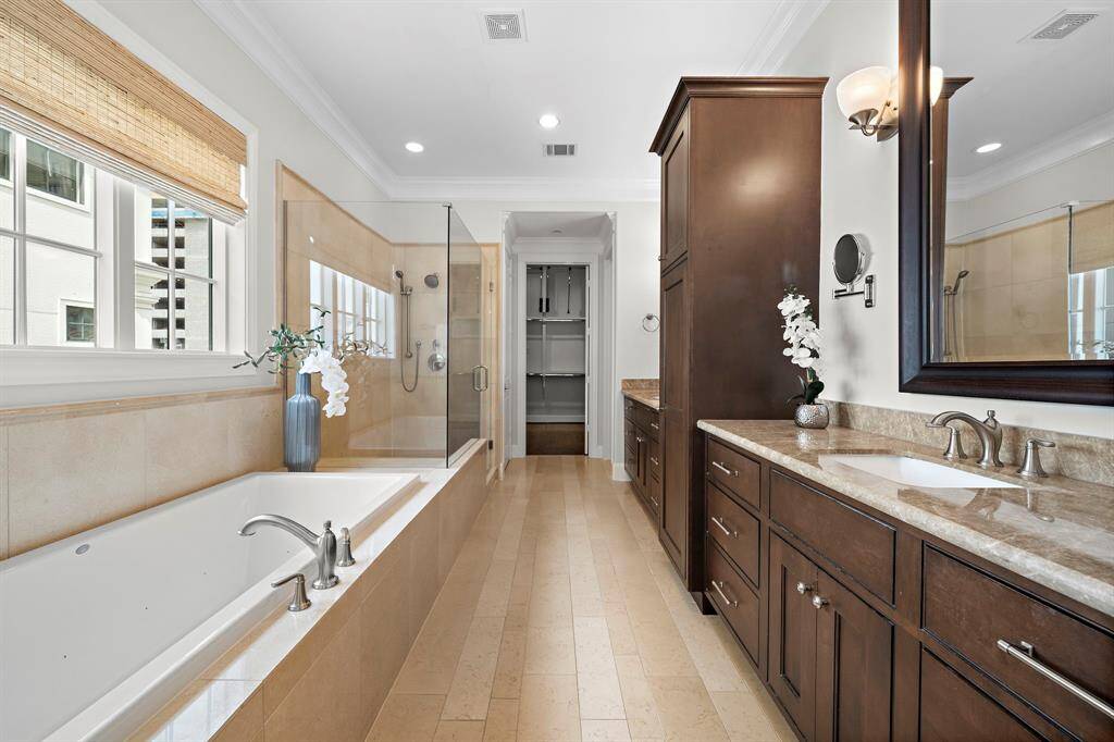 Indulge in spa-inspired luxury with a jetted soaking tub, walk-in glass shower, and dual vanities topped with elegant stone counters. Custom cabinetry, high-end designer fixtures, and direct access to an expansive walk-in closet complete this serene and sophisticated ensuite retreat.