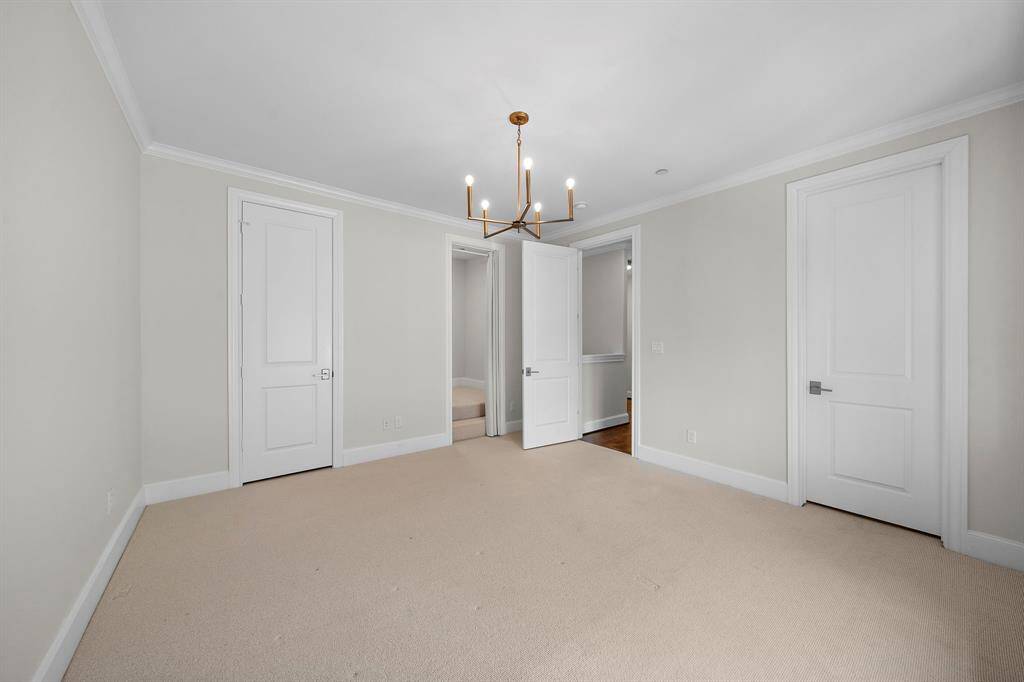 Spacious secondary bedroom blends plush carpeting with elegant crown molding and a statement gold chandelier, creating a restful ambiance. Three doors offer access to an ensuite bath, walk-in closet, and hallway, while the versatile layout delivers both privacy and flexibility for use as a guest suite or flex space.