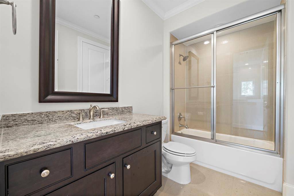 This beautifully appointed secondary bath features an oversized granite-topped vanity with ample storage and a sleek under-mount sink. A frameless glass-enclosed tub with a walk-in shower and neutral tilework combines style and function, delivering a refined retreat for guests or residents.