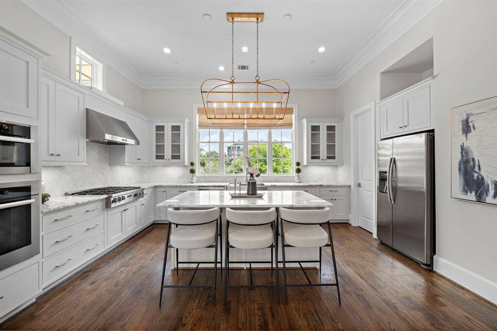 The gourmet kitchen is a showpiece with professional-grade stainless appliances, an oversized stone island, custom cabinetry, and designer backsplash. Expansive windows provide city views and abundant natural light, while soft-close drawers, a gas cooktop, and wine storage elevate the space for culinary excellence and sophisticated entertaining.