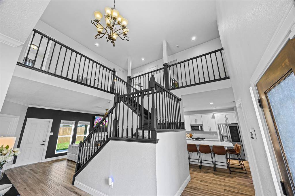 Striking two-story entry with modern black staircase, elegant chandelier, and open flow into a sleek white kitchen with breakfast bar seating. The updated kitchen is a chef’s dream with ample cabinetry, granite countertops, and a cozy breakfast nook overlooking the peaceful backyard. Step outside to a private patio ideal for grilling, relaxing, or future outdoor upgrades.