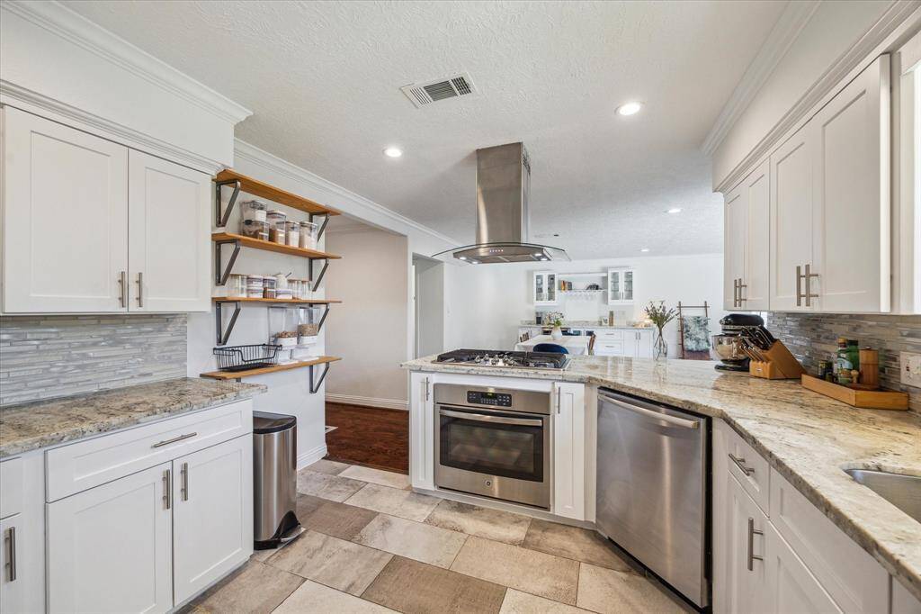 Kitchen view looking towards the home's dining room area.  Bosch Dishwasher, Wall Oven, 5 burner gas cooktop with an exhaust system that vents to the outside. Designer brushed nickel hardware, designer tile backsplash.