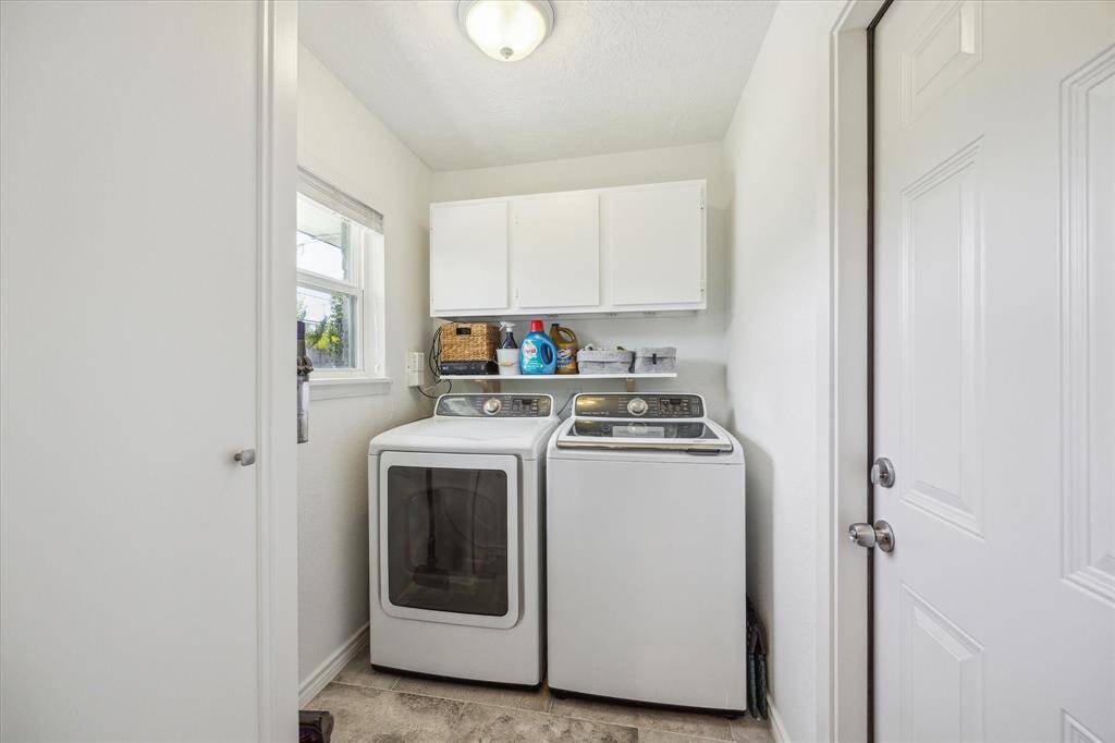 View of the homes in house utility room located off the home's kitchen.  Full size top loading washer and dryer fit perfectly plus built in storage above the washer and dryer.  There is a window in the utility room that looks out to the homes back yard area.  The door opens to the homes two car oversized garage.