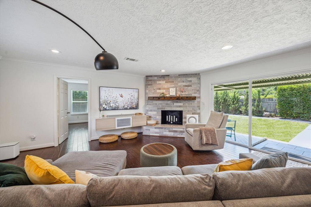 View of the home's living room area.  The door to the left opens to the home's primary suite which is placed at the back of the home. Beautifully tiled fireplace with wood beam mantle. Sliding glass door opens to the homes 16x7 covered patio and great backyard area perfect for kids and pets.