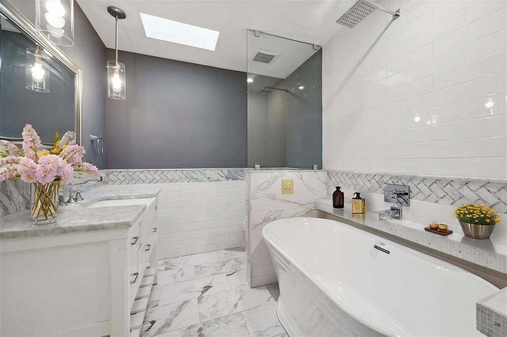 The hall bathroom has a sky light for natural light, has been completely remodeled. Stand alone tub, marble like tile, shiny subway tile, and a marble counter top.