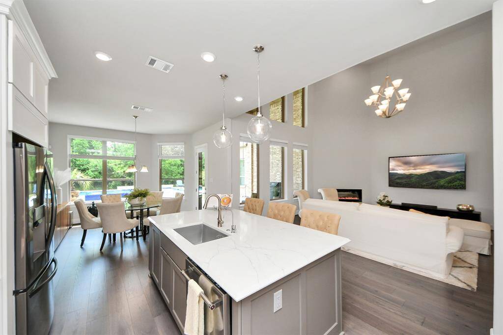 This bright and modern open-concept kitchen, breakfast room and living area features high ceilings, and a large center island with marble countertops. The space is illuminated by stylish pendant lighting.