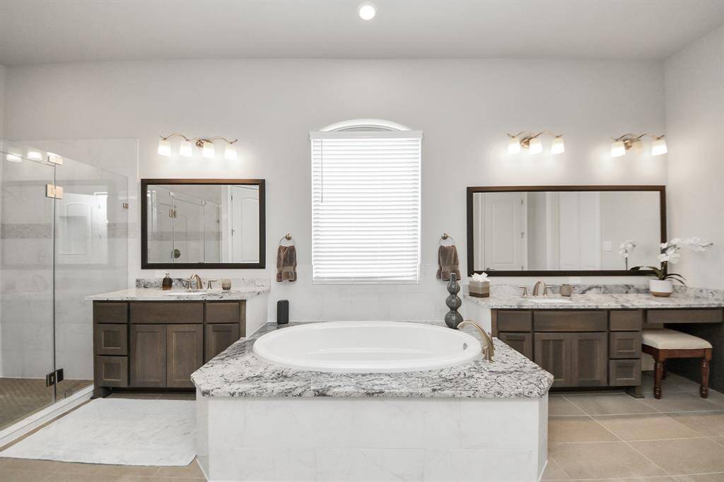 This primary bathroom offers a simple and practical setup with double sinks, a soaking tub, and a separate shower. There's also a built-in vanity area with a spot to sit and get ready.
