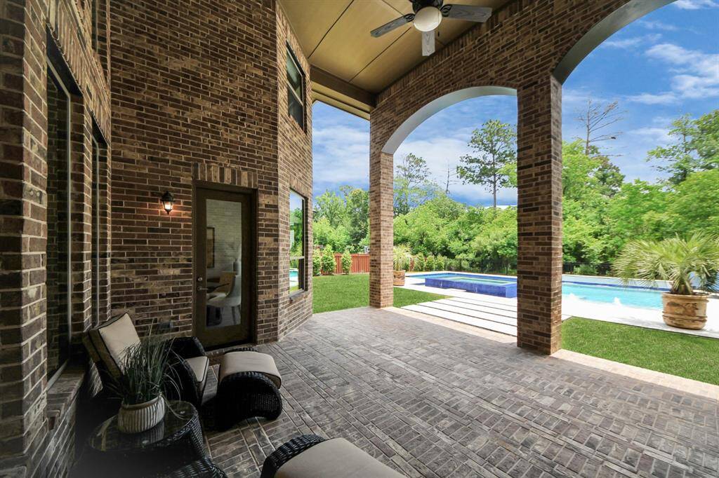 A high ceiling, covered patio with brick detailing, overlooking a lush backyard with a pool. The area features comfortable seating and ceiling fans, ideal for outdoor relaxation and entertaining.