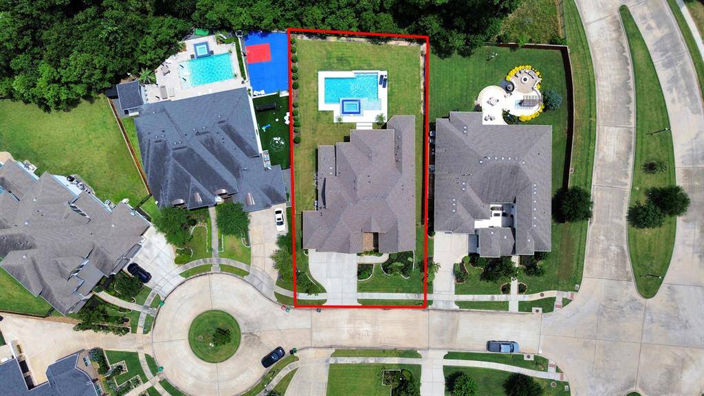 This aerial view showcases a row of spacious, well-maintained homes in a lush, green neighborhood. The properties feature large driveways, manicured lawns, and are bordered by trees, offering privacy and a serene environment.
