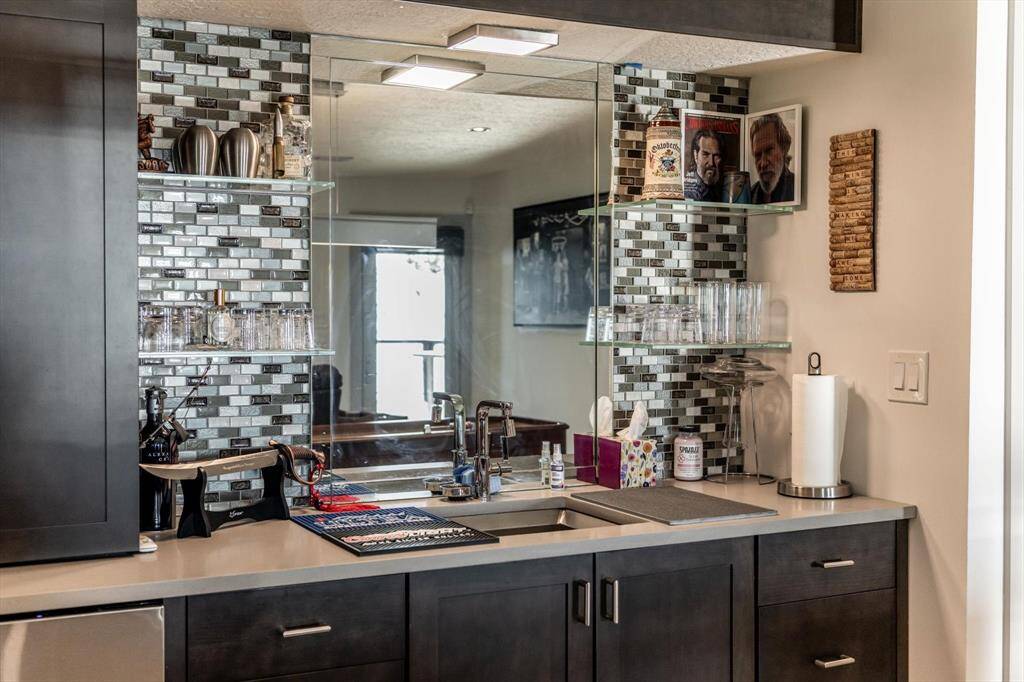 Cheers to a night in—this sleek wet bar with mirrored backsplash and glass shelving is ready for cocktails, conversation, and a round of shuffleboard.