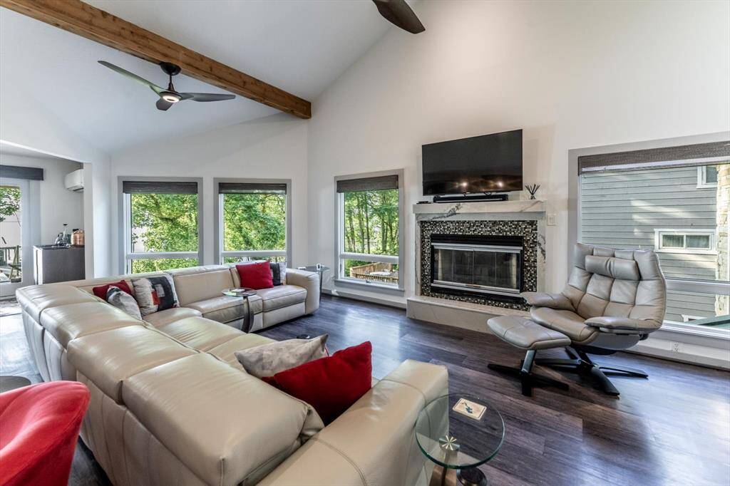 The fireplace and tall ceilings with wood beams frame this stylish and modern living room with a wall of windows overlooking the lake.