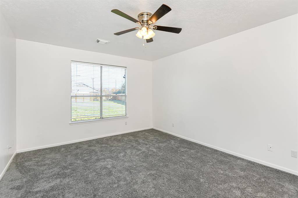 This bright, spacious room features fresh carpeting and a large window, offering plenty of natural light and a serene view—perfect for a cozy bedroom or home office.