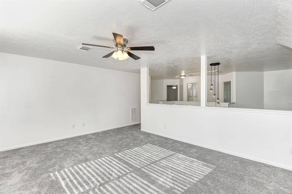 Spacious and bright living area featuring plush carpet, modern ceiling fan, and elegant lighting fixtures. Perfect for relaxation and entertaining.