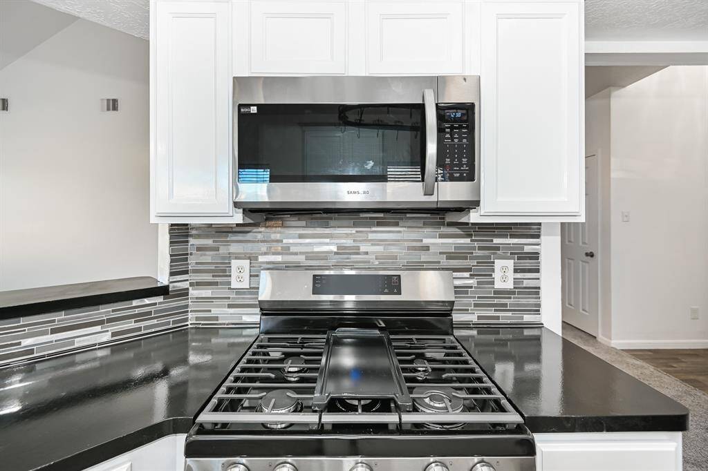 Modern and sleek kitchen featuring a stainless steel oven and microwave, complemented by stylish white cabinetry and a chic tile backsplash. Perfect for culinary enthusiasts.