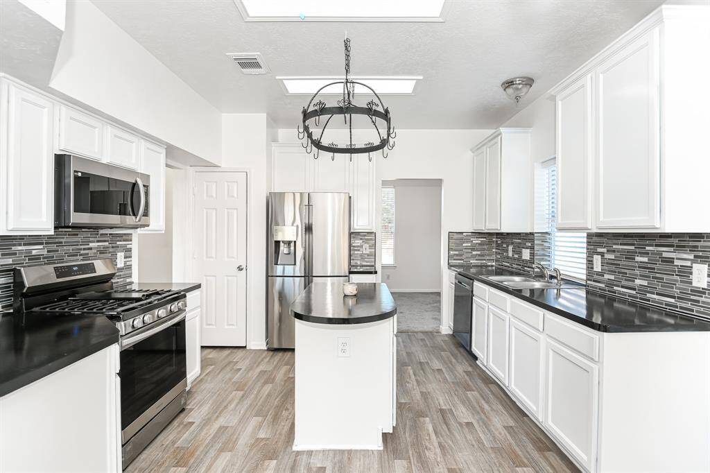 Modern kitchen featuring sleek stainless steel appliances, elegant white cabinetry, and a stylish backsplash. The center island offers additional workspace, complemented by abundant natural light and a contemporary chandelier. Perfect for culinary enthusiasts and entertaining.
