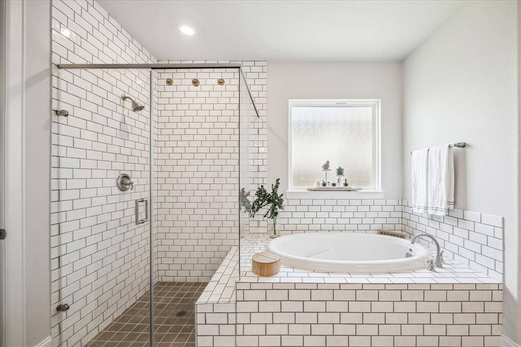 Primary shower with convenient bench, seamless glass and soaking tub with upgraded tile surround.