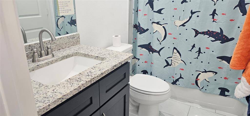 Hall bath with granite countertops, tub/shower combo, along with an oval-shaped commode.
