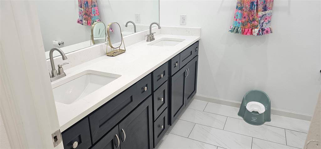 Well-lit owner's private bath with spacious quartz vanity, double undermount sinks, and tile flooring