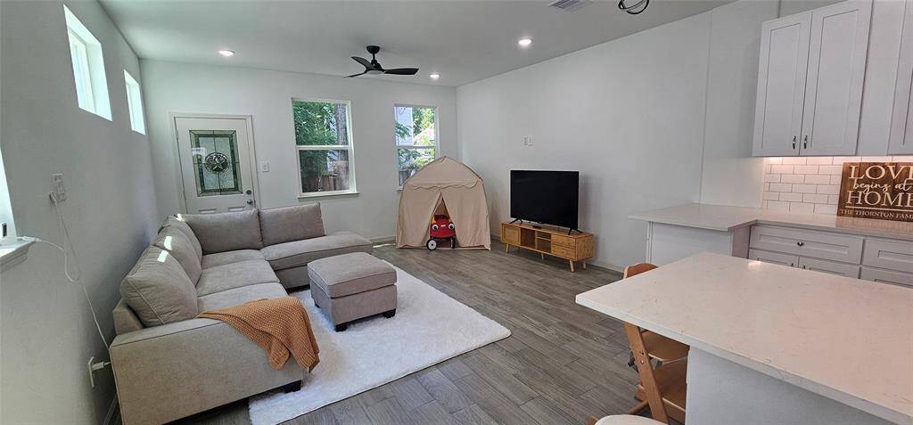 As you enter your home, you are welcomed by a bright open-concept living room, kitchen, and dining area with clean, neutral colors, with large windows allowing plenty of natural light. The open layout connects to a kitchen/dining area with white cabinetry and a contemporary quartz countertop.
