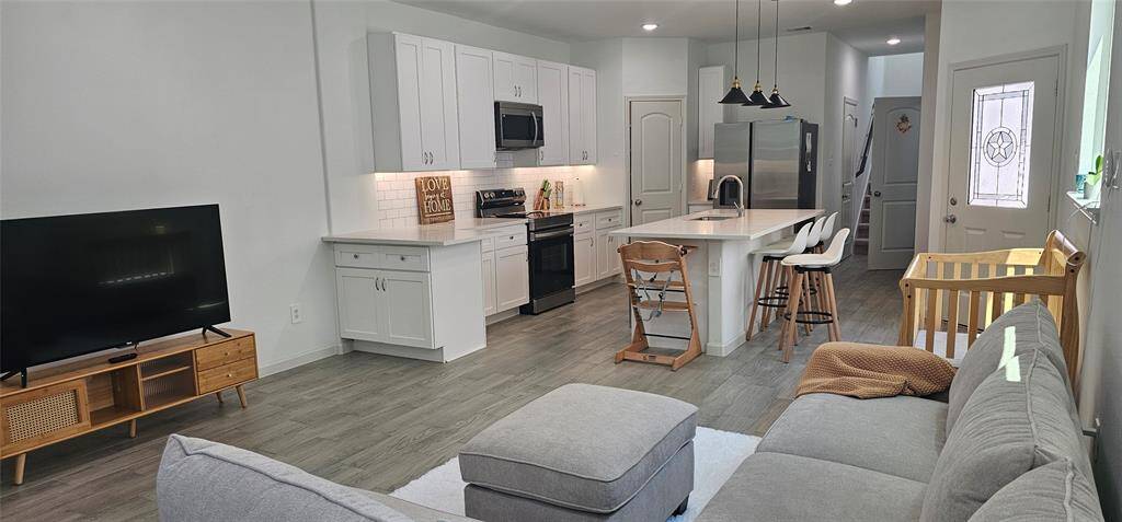 open-concept living space features a sleek kitchen with white cabinetry, stainless steel appliances, and a central island with dining bar. The adjoining living area is complemented by wood-like vinyl plank flooring and ample natural light.