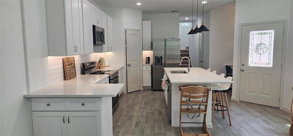 The kitchen features sleek white cabinetry, stainless steel appliances, and a central island. The wood-looking vinyl plank flooring adds warmth, while pendant lighting provides a stylish touch. The space is bright and inviting, with ample countertop space for cooking and entertaining.