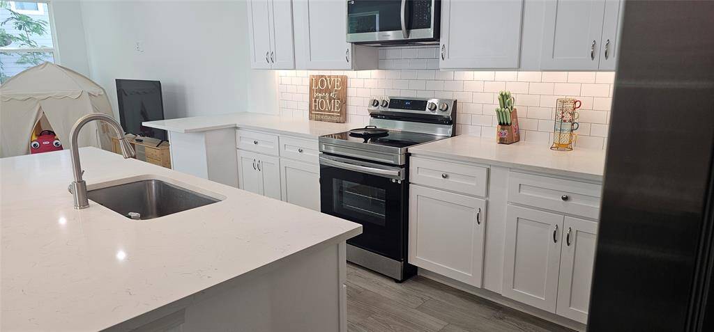 Another angle of the kitchen featuring white cabinetry, like-new stainless steel appliances, and a spacious island with an undermount sink. The backsplash is a classic white subway tile, providing a clean and bright look. The abundance of counter space is ideal for both cooking and entertaining.