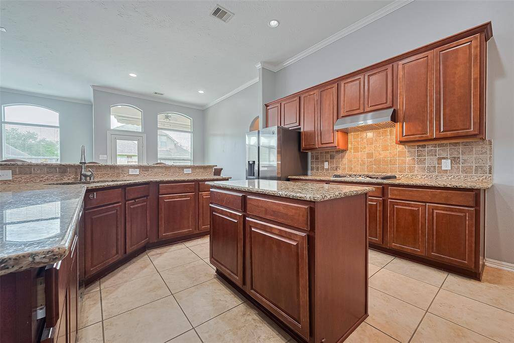 This spacious kitchen features rich wooden cabinetry, granite countertops, and a chef's island. It offers stainless steel appliances, a tile backsplash, and plenty of natural light from large windows, creating an inviting and functional cooking space.