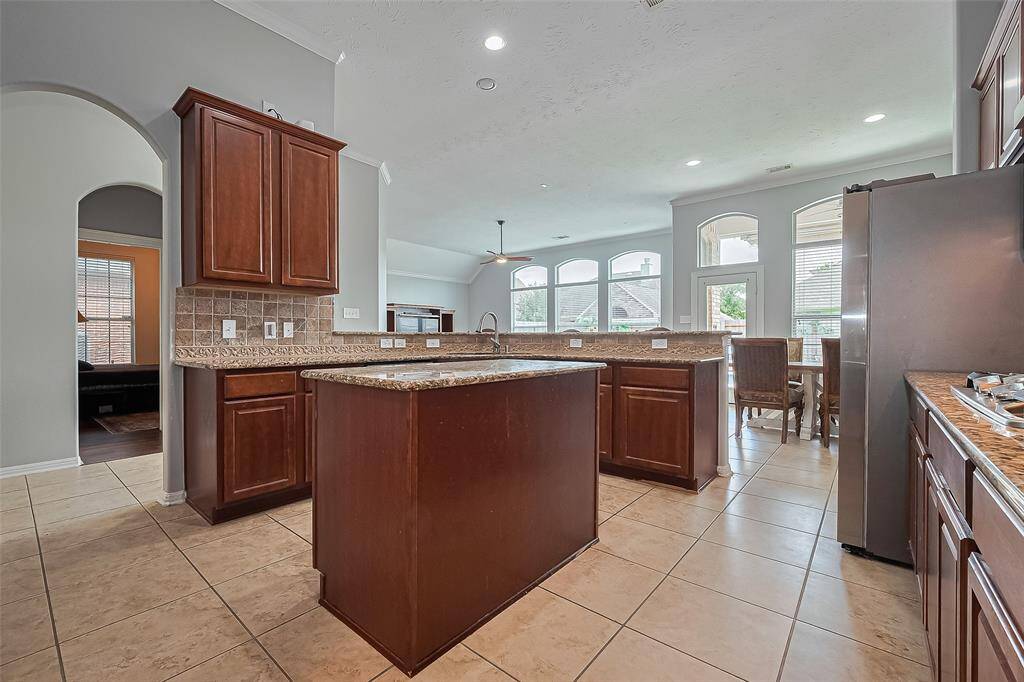 This spacious kitchen features elegant wooden cabinetry, granite countertops, and a central island. Large windows provide ample natural light, and the open layout flows seamlessly into the dining area.