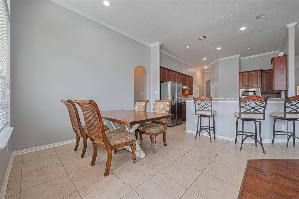 This photo showcases a spacious kitchen and dining area with modern amenities. The room features a breakfast bar with seating, stainless steel appliances, and ample natural light. The neutral color palette and tiled flooring create a welcoming atmosphere, perfect for family gatherings.