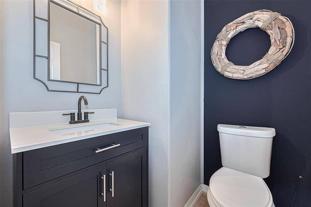 This photo showcases a modern half bathroom with a sleek vanity featuring an updated cabinet and white stone countertop.