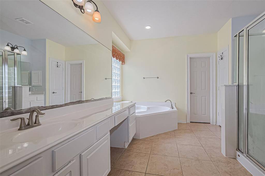 This bathroom features a spacious layout with dual sinks and vanity, corner soaking tub, and a separate glass-enclosed shower.