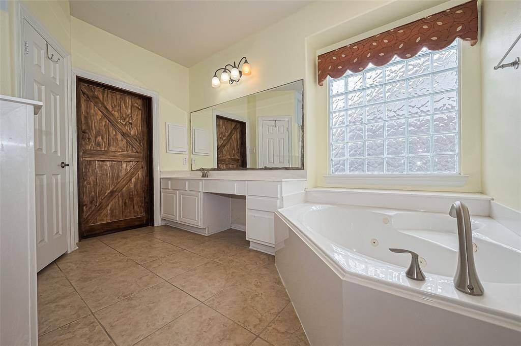 This bathroom features a spacious layout with a large corner whirlpool tub, a wide vanity with ample storage, and a rustic wooden barn door.