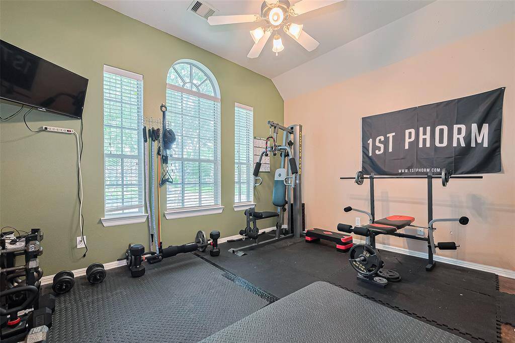 One of three secondary bedrooms, currently set up as a home gym. This room features large windows for natural light, a ceiling fan, and a mounted TV (included).