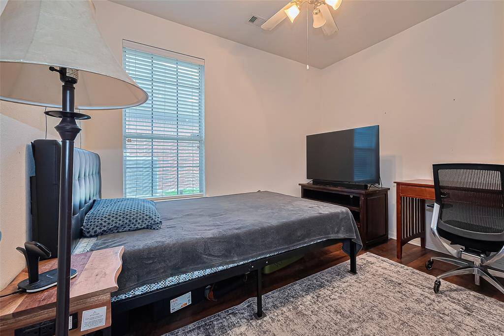 This cozy bedroom offers a large window for natural light, a ceiling fan, warm engineered wood flooring, and a walk-in closet. An additional secondary bedroom is also included (not pictured).