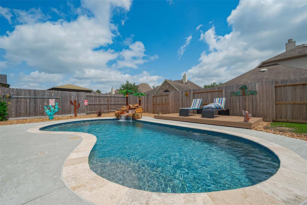 This backyard boasts a beautifully designed pool with a stone waterfall and a spacious deck area with lounge chair area—perfect for relaxing. The fenced yard and simple landscaping create a private, serene outdoor oasis.