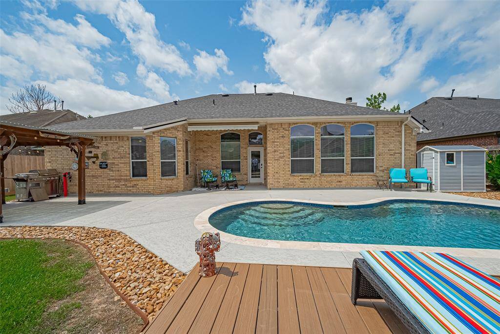 This backyard offers a spacious patio with a pergola, a well-maintained pool, and inviting seating areas. The full brick back exterior complements the lush landscaping, creating a peaceful and elegant outdoor retreat.