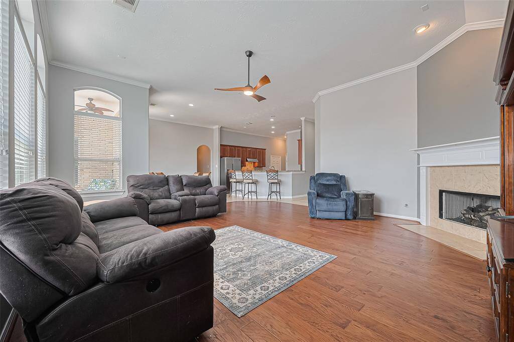 This spacious living area features engineered  hardwood floors, a cozy fireplace, and abundant natural light from large windows. An open layout connects seamlessly to the kitchen, which includes a breakfast bar. The room is perfect for comfortable living and entertaining.