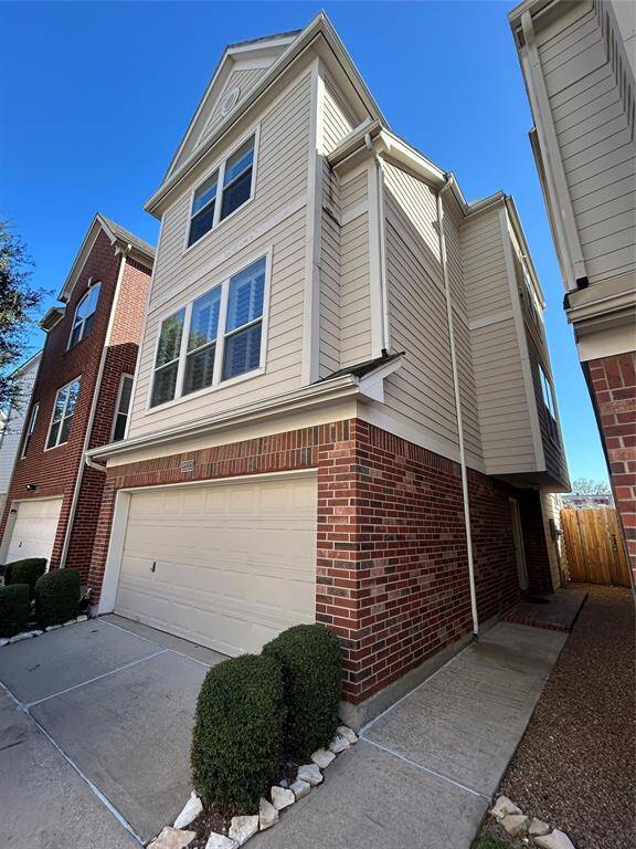 This is a modern, three-story townhouse with a brick and siding exterior. It features a two-car garage, large windows, and a well-maintained driveway. The house is part of a cluster of similar homes, offering a neat and contemporary look.