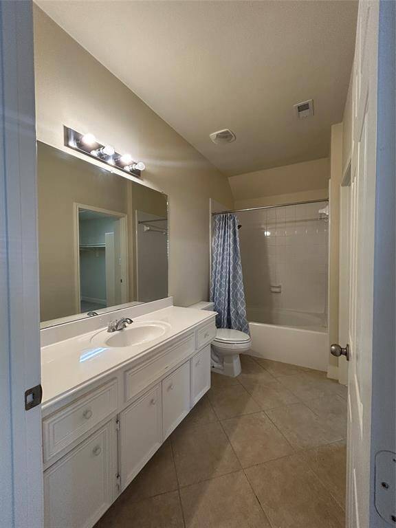 This bathroom features a large vanity with ample storage, a wide mirror, and overhead lighting. It includes a combo shower and bath.