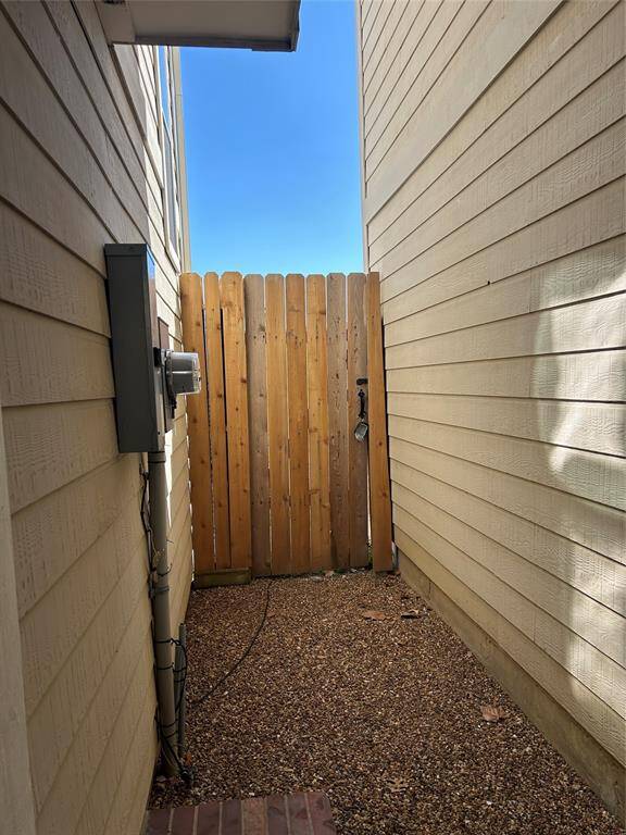 Side yard with pebble ground covering. It features a wooden gate at the end, providing access and natural light.