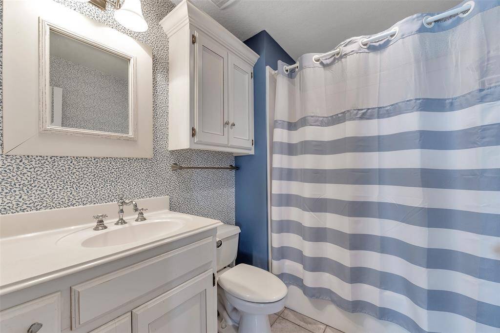 Full bath features a classic tub/shower combo, tile flooring, and linen cabinetry for extra storage. Clean, coastal, and ready for everyday comfort or guest use.