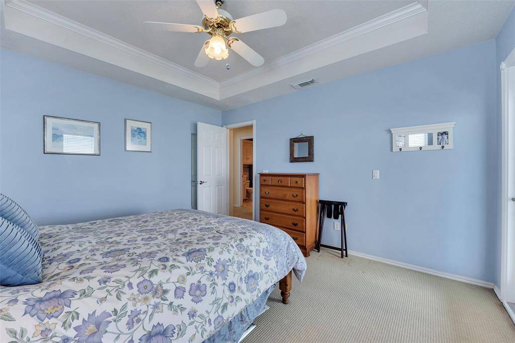 Soft blue walls and neutral flooring create a calming atmosphere in this secondary bedroom. The tray ceiling adds architectural interest while the layout offers ample space and flow to the adjoining bath.