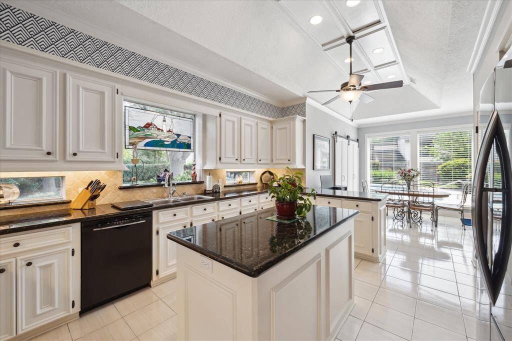 The kitchen includes a center island and a large window that overlooks the backyard. The counter tops are granite and accented with travertine backsplash. Travertine wrapped transom windows in the backsplash wall are trimmed with matching granite sills and allow natural light to enter. Under cabinet lighting highlights these features.