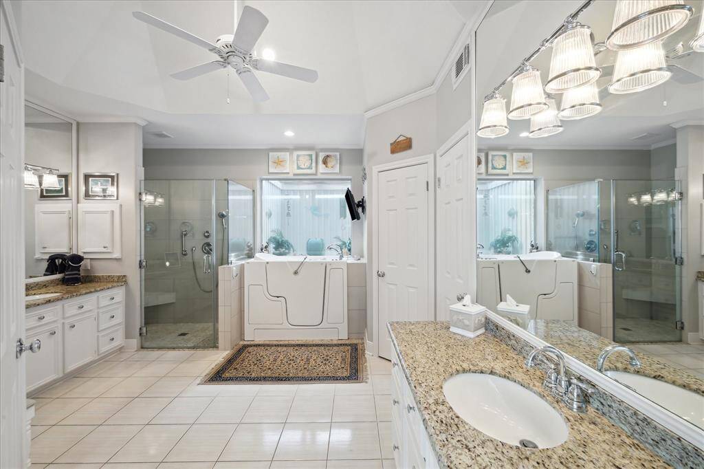 The view when entering the en-suite primary bath. Split vanity cabinets with granite tops and undermount sinks, ceramic tile floor, updated shower with tile surround, double soap niche, corner bench and frameless glass surround and double closets are features of this bathroom.
