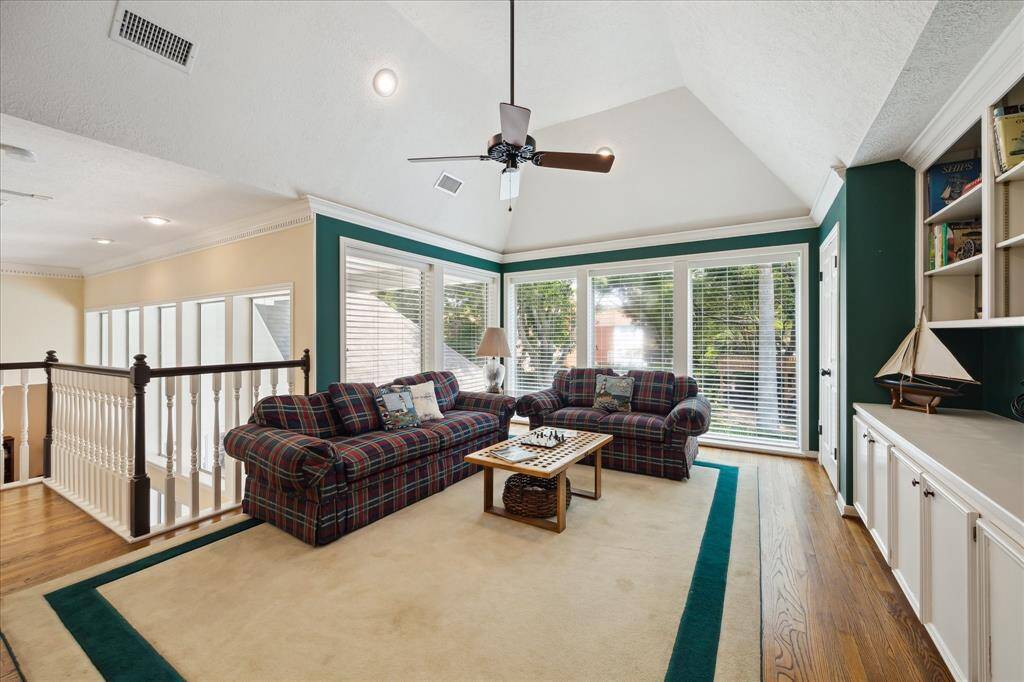 This view across the game room shows the wall of windows overlooking the backyard and pool as well at the banister railing overlooking the main entry to the home.