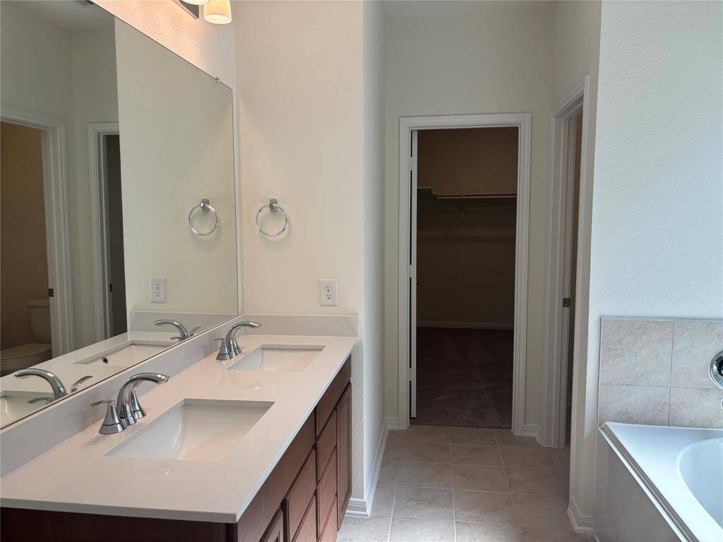 Modern Primary bathroom featuring a double sink vanity, large mirror, and a spacious walk-in closet. Neutral tones and tile flooring add a clean, elegant touch.